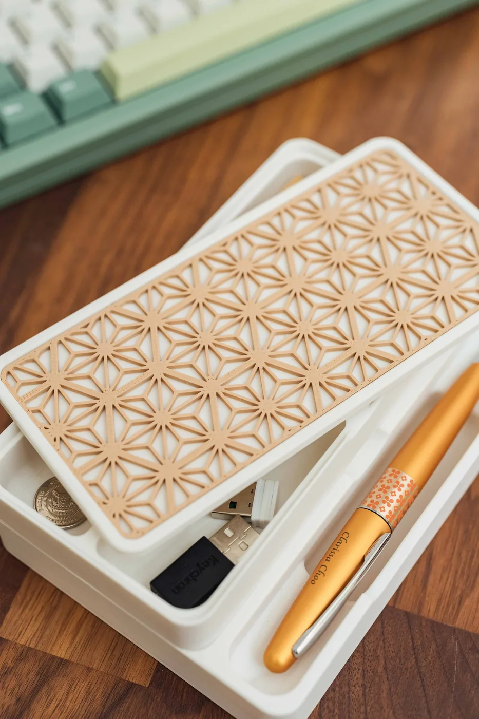 A white desk organizer containing a gold pen, USB drives, and coins, placed on a wooden surface with a keyboard in the background.